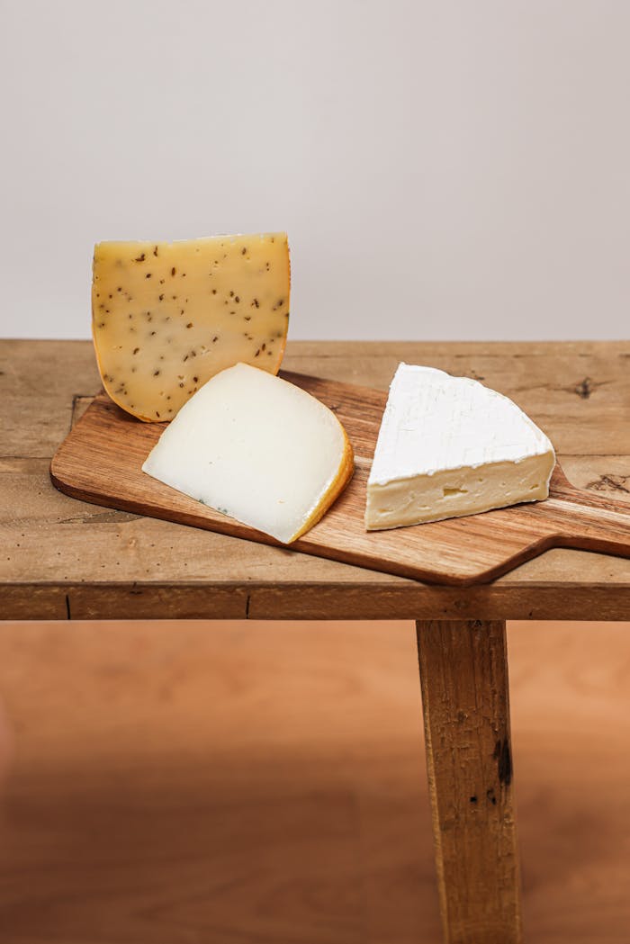 Three types of gourmet cheese displayed on a wooden chopping board, perfect for culinary enthusiasts.