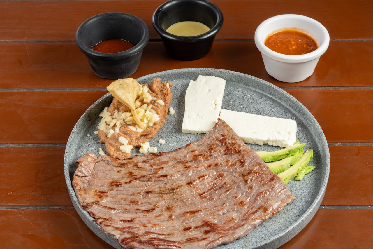 Delicious grilled skirt steak served with Mexican-style side dishes including cheese, refried beans, and sauces.